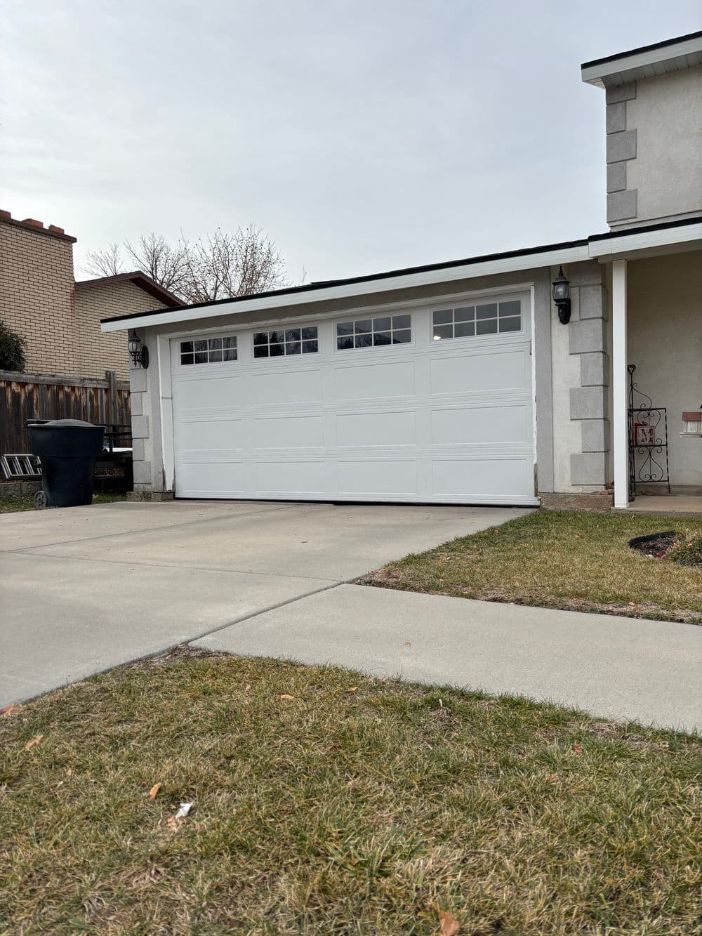 White garage door with windows, concrete driveway, and grassy area near a suburban home.