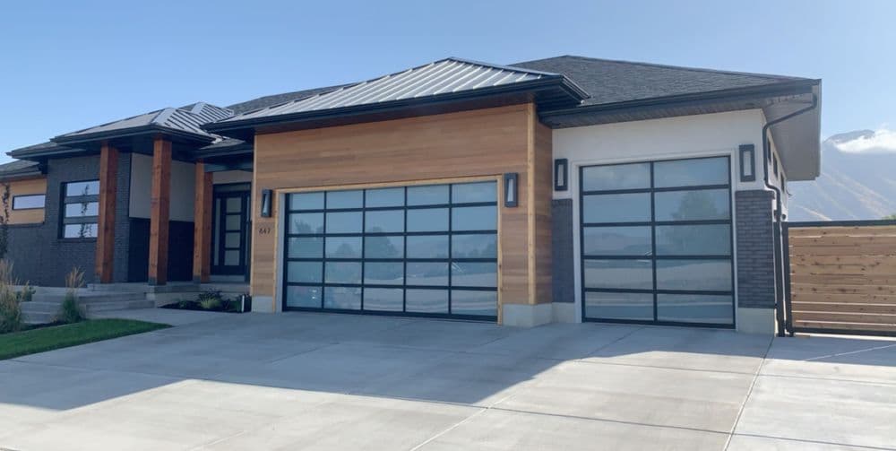 Modern house with wooden accents and large glass garage doors against a clear blue sky.