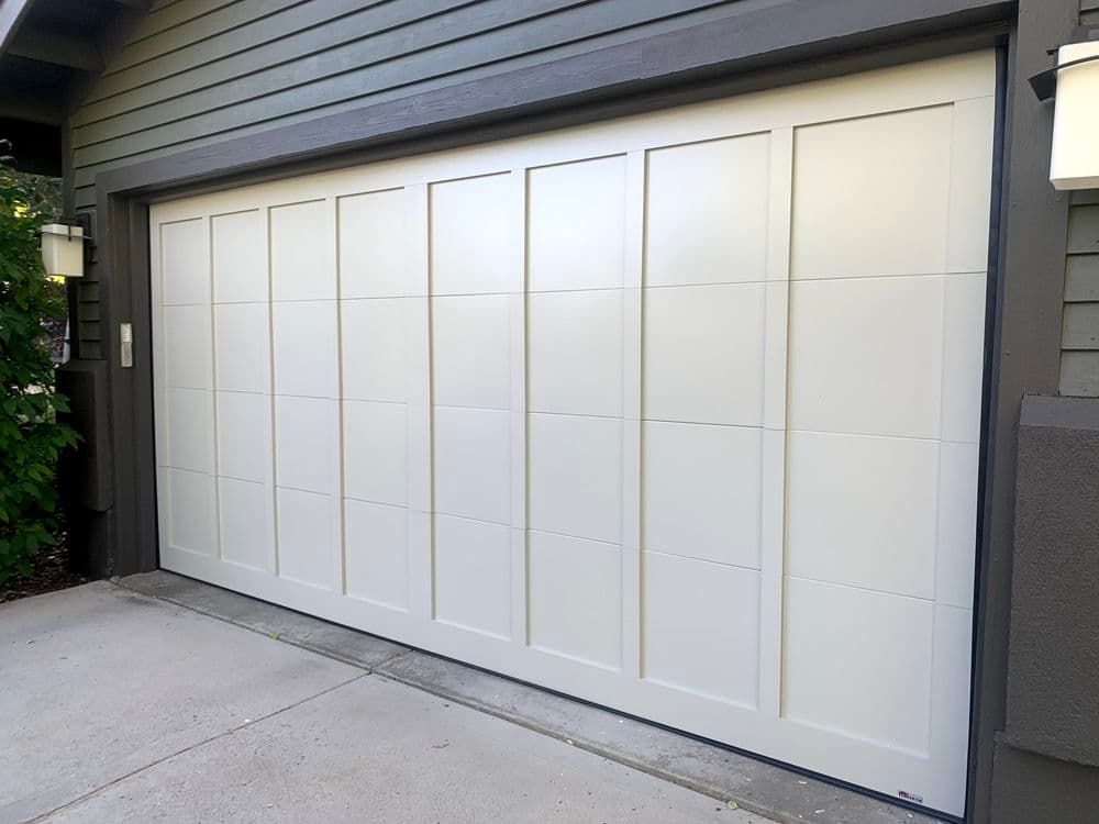 Modern white garage door with a panel design, set against a gray house exterior.