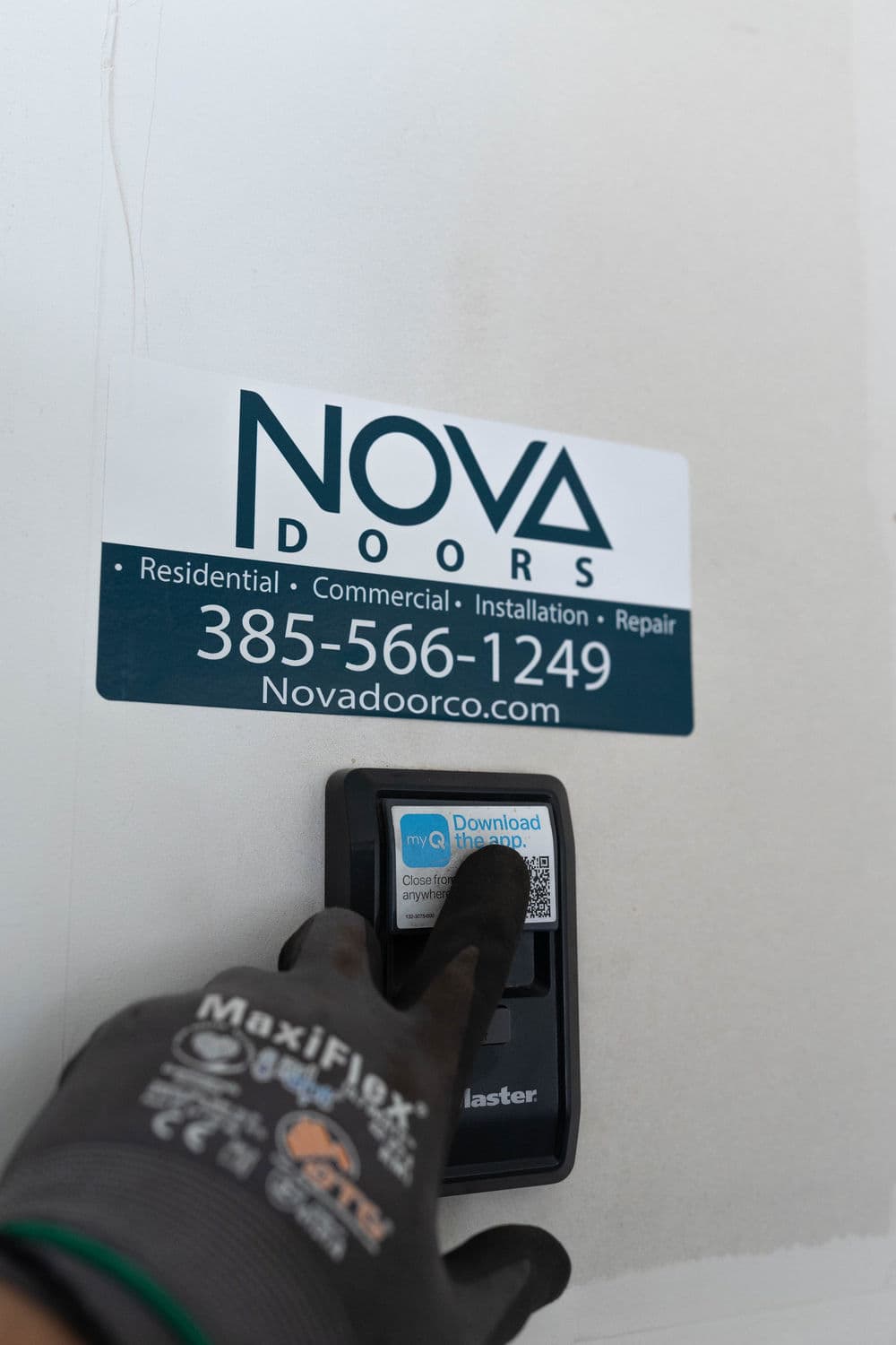 Hand pressing a smart door access panel with Nova Doors contact information and QR code.