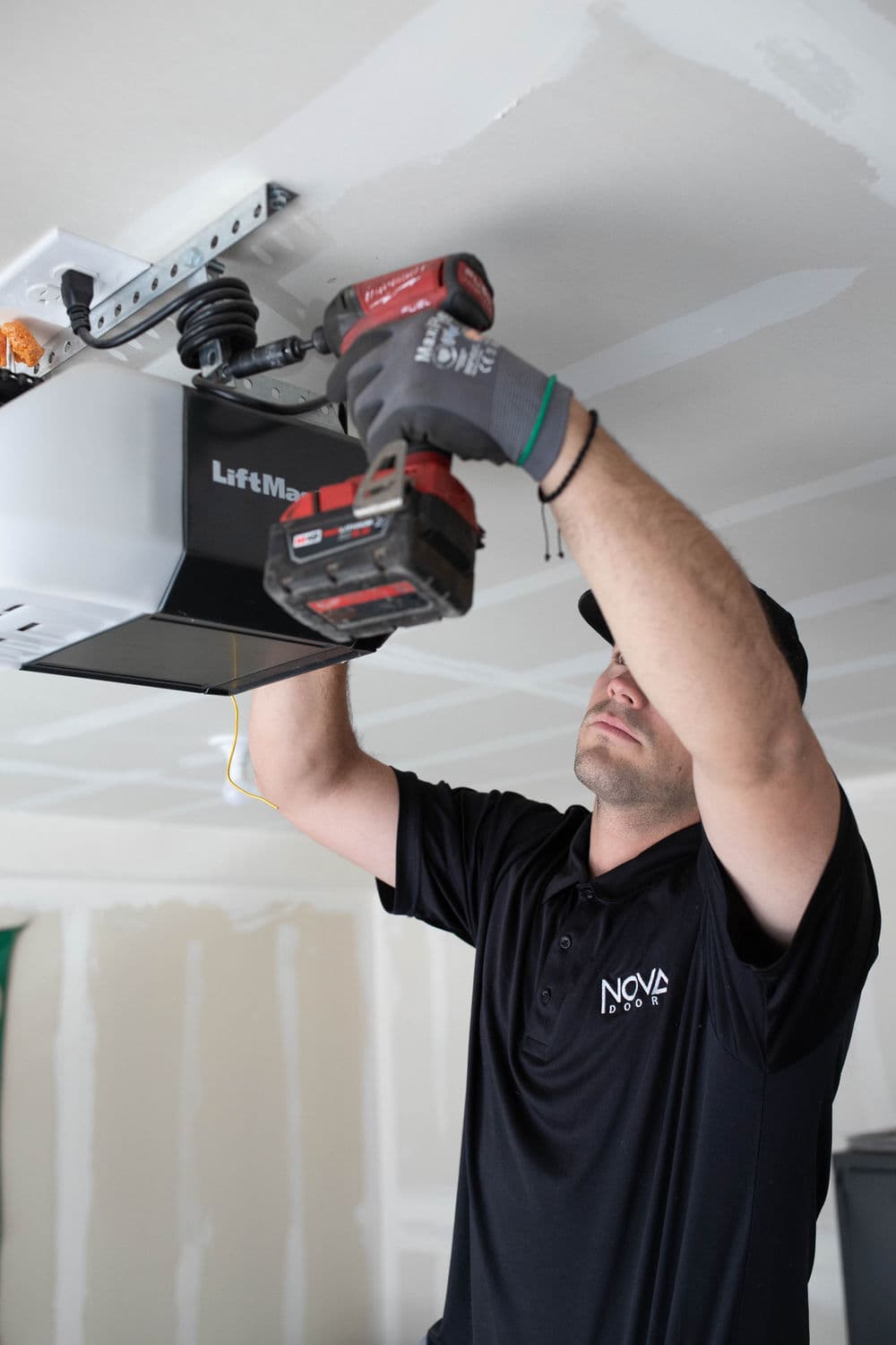 Technician installing LiftMaster garage door opener using power drill in garage.
