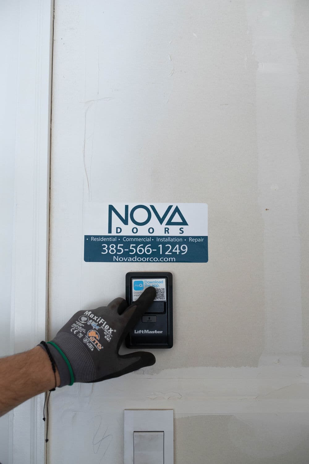 Hand reaching for a LiftMaster control panel beside NOVA Doors service sign on a wall.