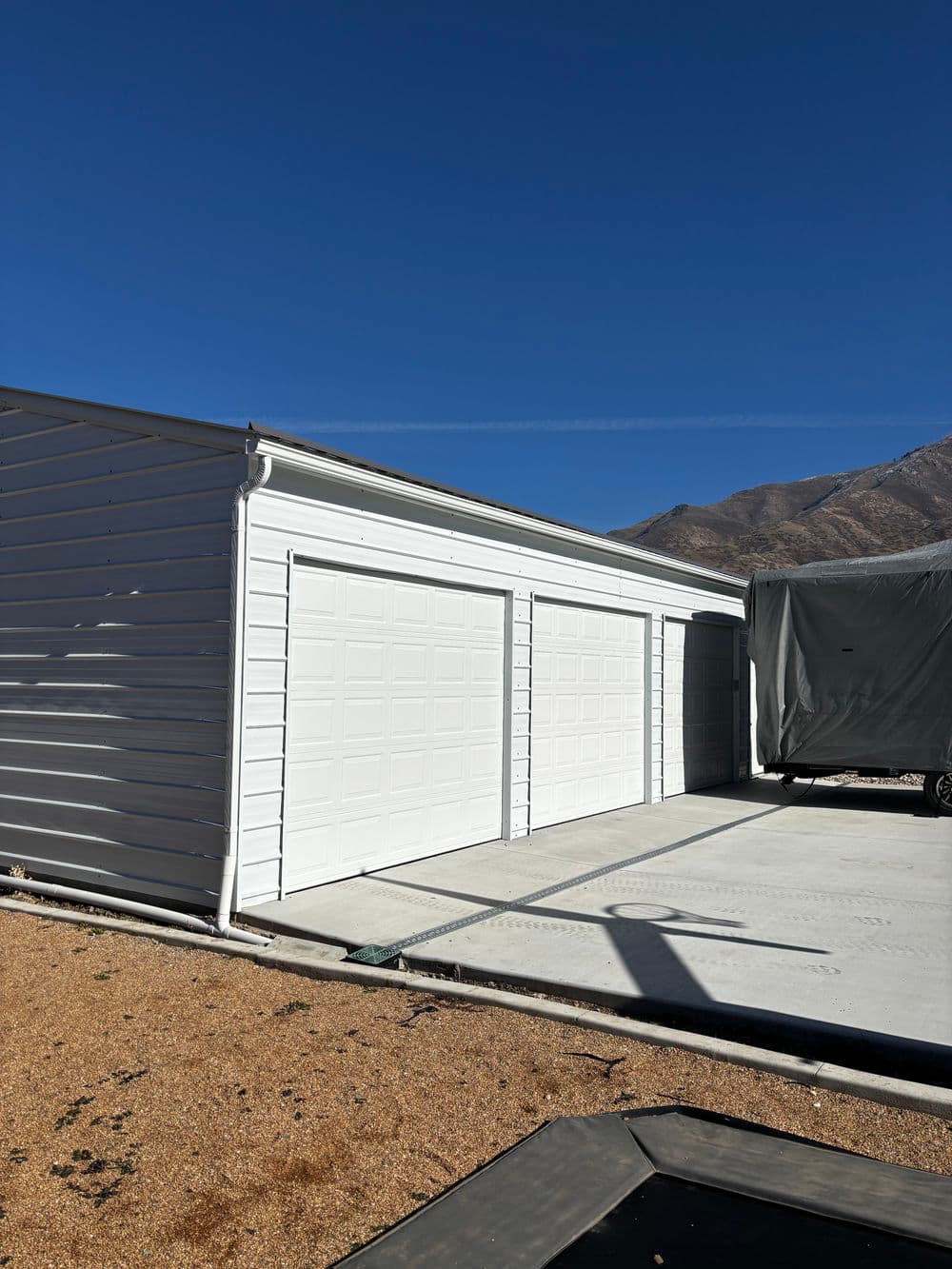 Modern metal garage structure with two doors and mountain backdrop under clear blue sky.