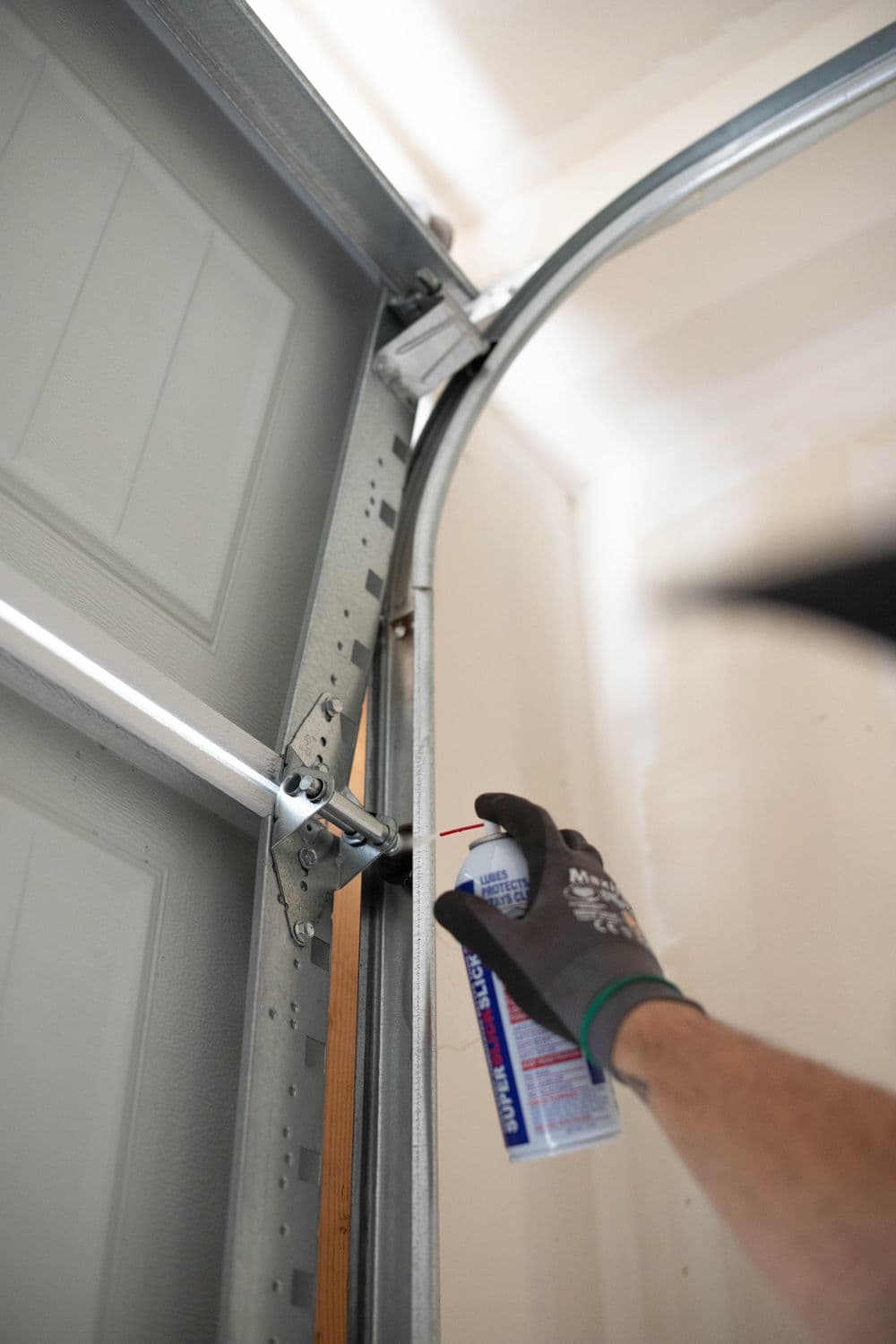 Person lubricating garage door track with spray lubricant for maintenance.