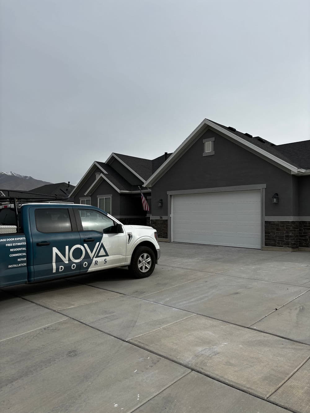 NOVA Doors vehicle in front of a gray house with a garage door and mountain backdrop.