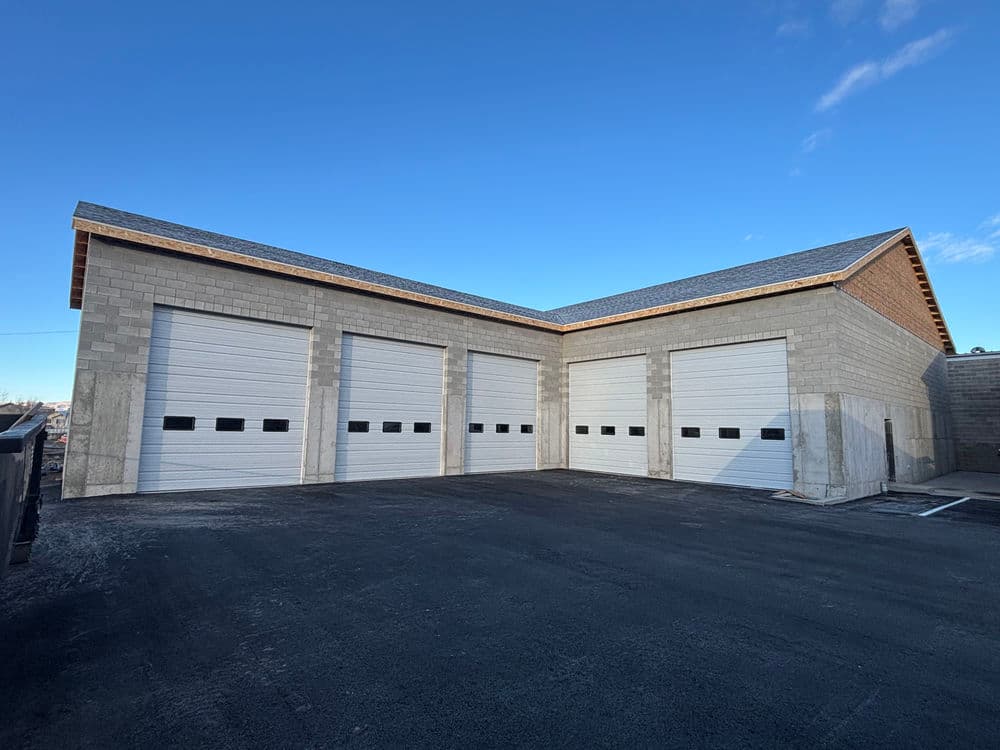 Modern storage facility with three white overhead garage doors and clear blue sky.