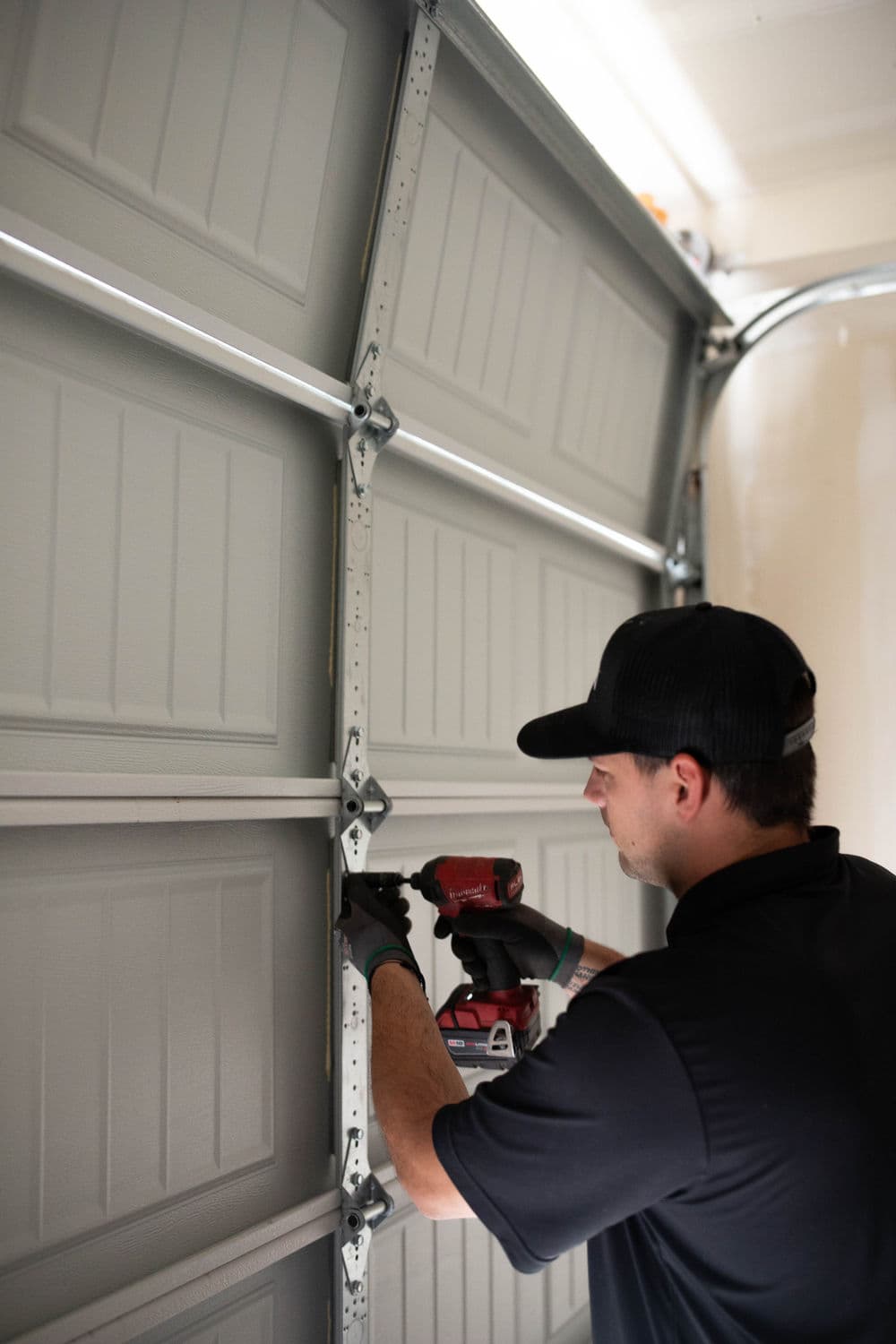 Man using a power drill to install a garage door panel. Bright garage setting.
