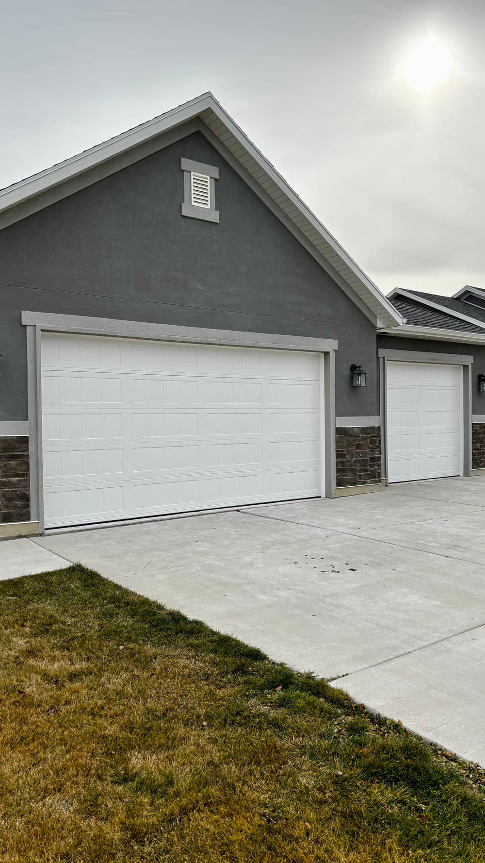 New residential garage with two white doors and stone accents on a concrete driveway.