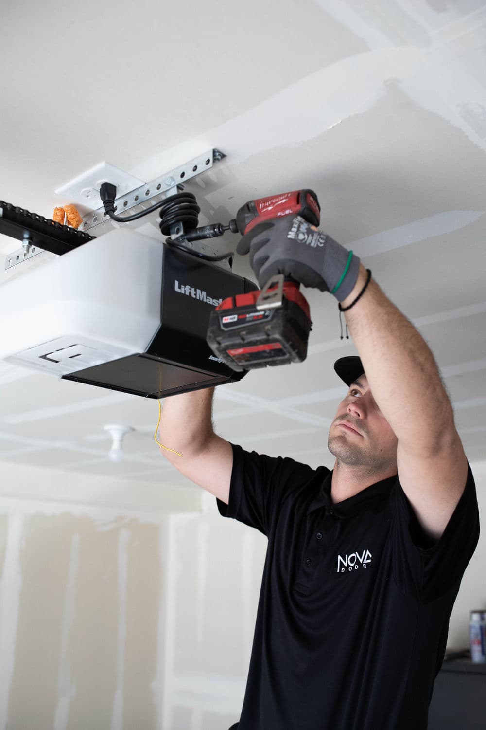 Technician installing LiftMaster garage door opener with power tools in residential garage.