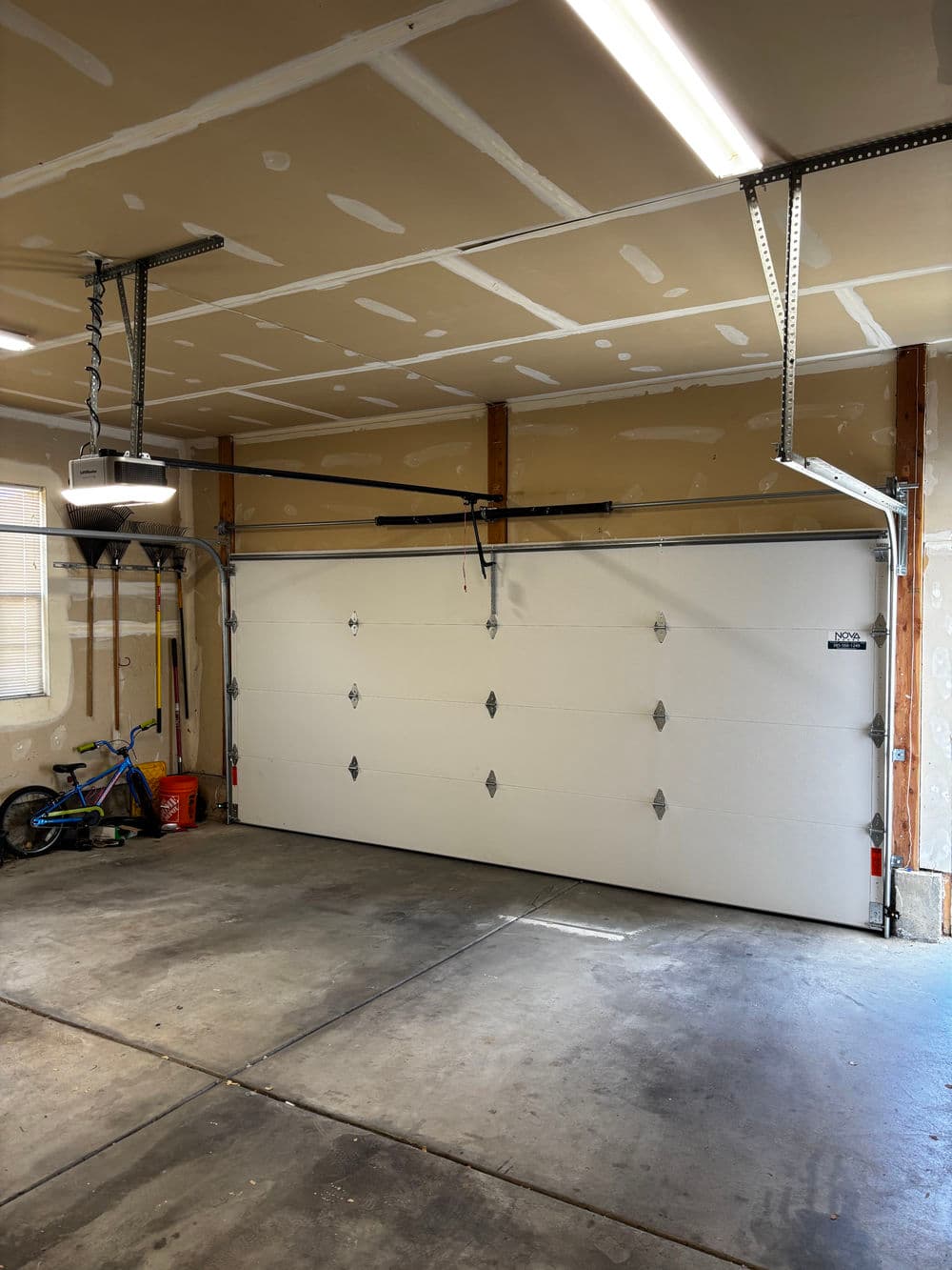 Garage interior with roller door, bike, and overhead lighting in an unfinished space.
