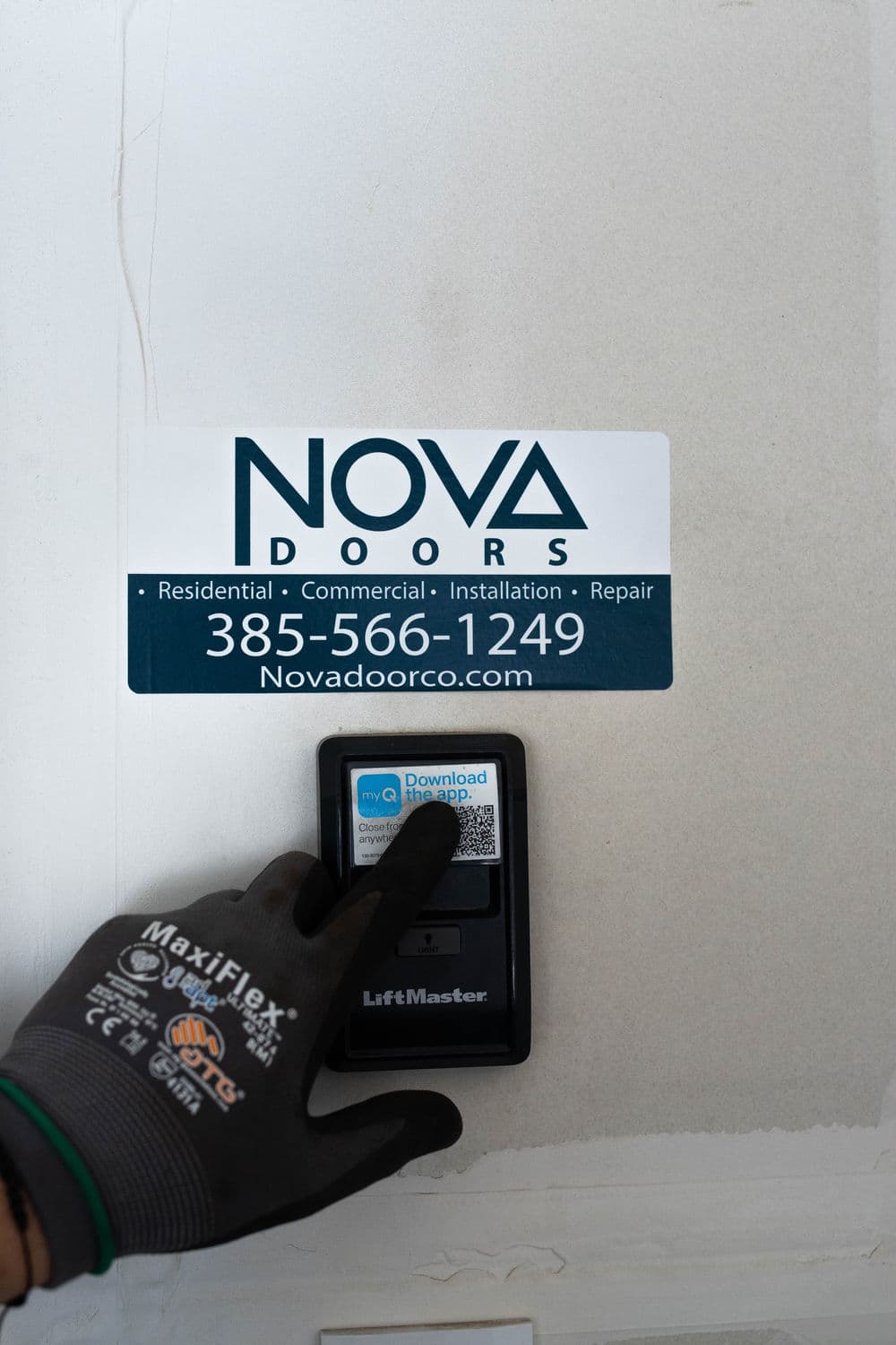 Hand using LiftMaster controller on Nova Doors service sign with contact information.