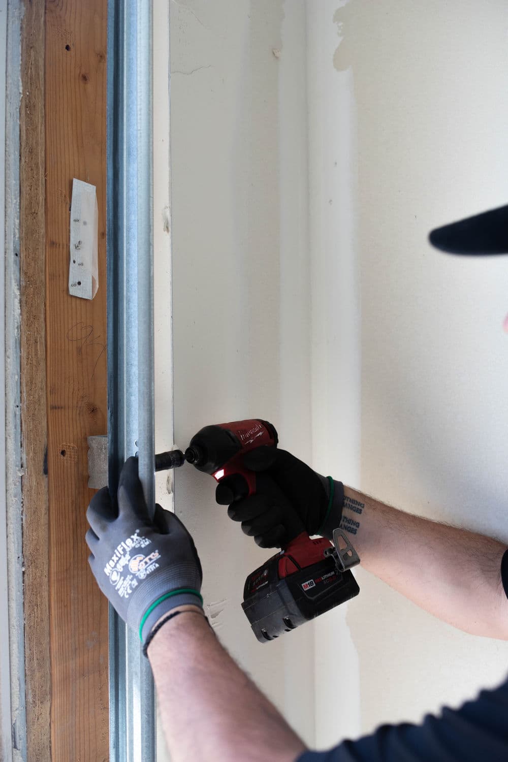 Person installing hardware with a power drill, wearing gloves in a home renovation setting.