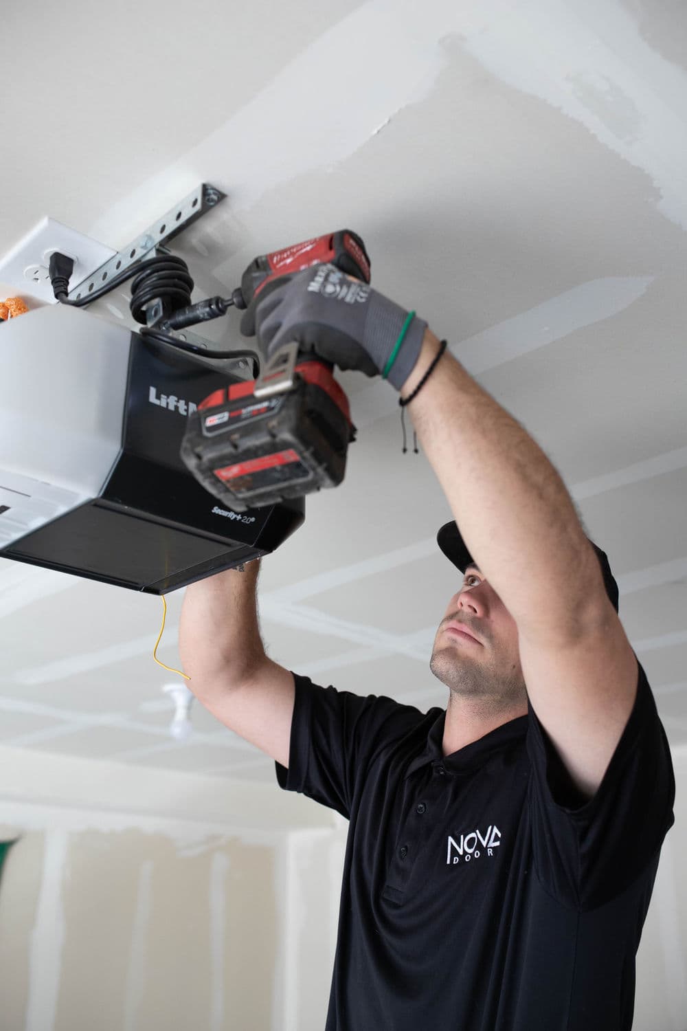 Technician installing a LiftMaster garage door opener using a cordless drill.