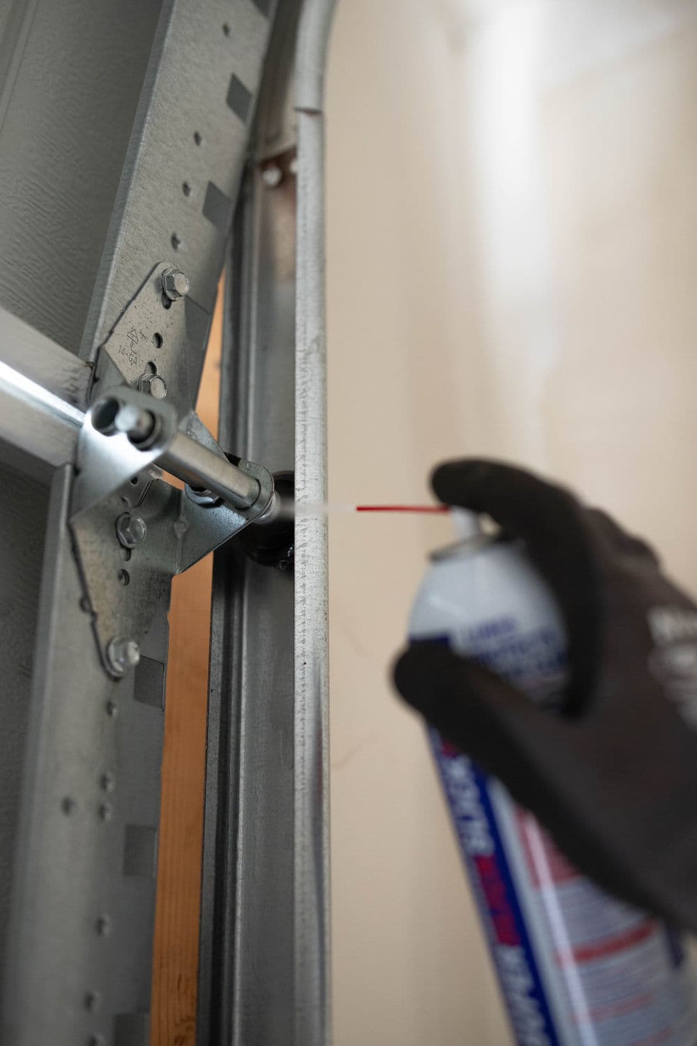 Person lubricating garage door track with spray lubricant for maintenance.