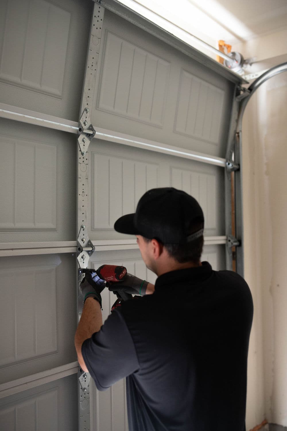 Garage door repair technician using a power drill to fix the door mechanism indoors.