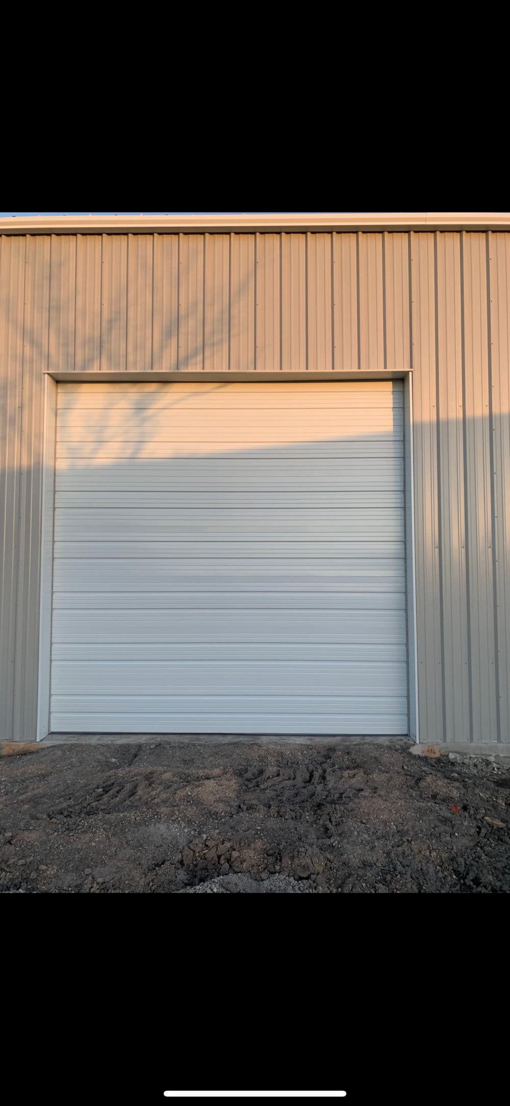 White garage door on a metal building with natural lighting and dirt ground.
