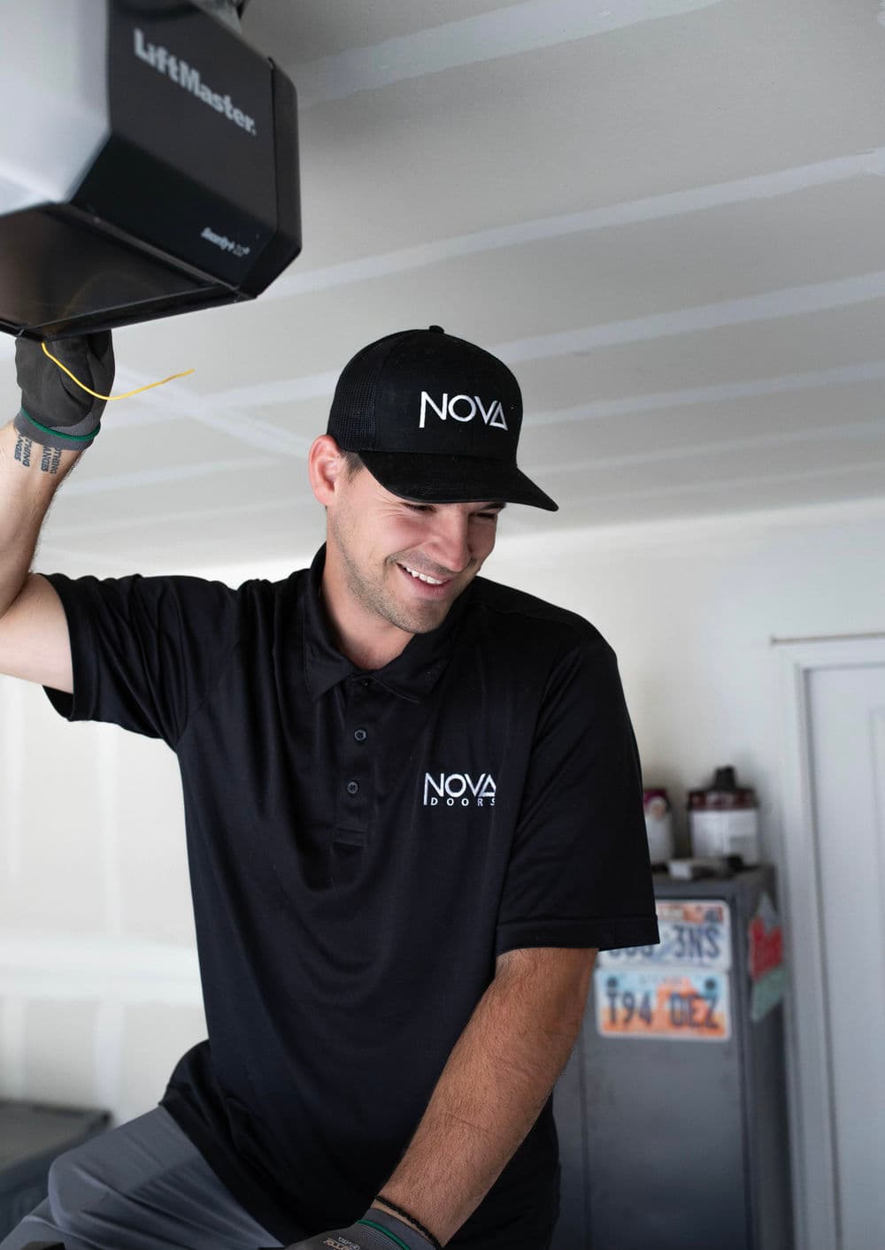 Smiling technician in black polo and cap, working on LiftMaster garage door opener.