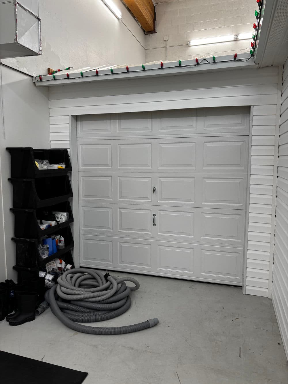 White garage door in a clean garage space with storage bins and a vacuum hose.
