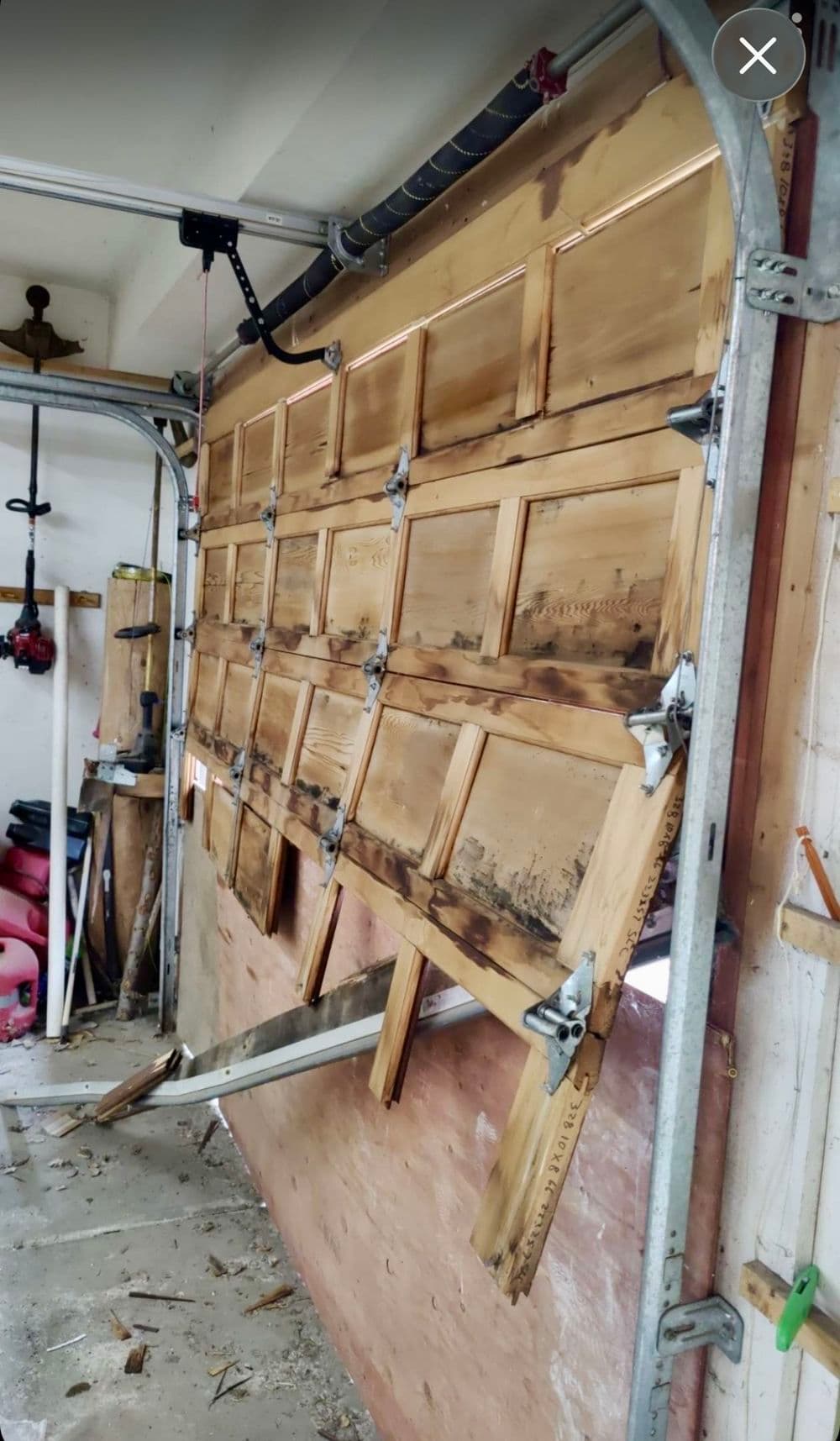 Damaged wooden garage door partially opened in a workshop environment.
