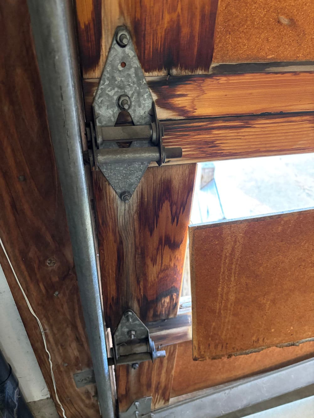 Close-up of rustic wooden door hinge with metal hardware and weathered wood detail.